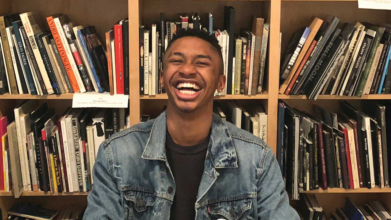 A photo of Tyler White seated in a library, laughing.