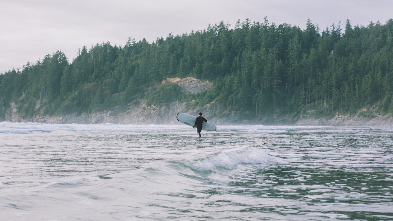 A person holding a surfboard wades into the ocean at a beach in Oregon's Oswald West State Park.