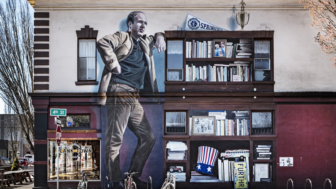 A photo of a two-story mural depicting author Ken Kesey leaning against a shelf of books and memorabilia