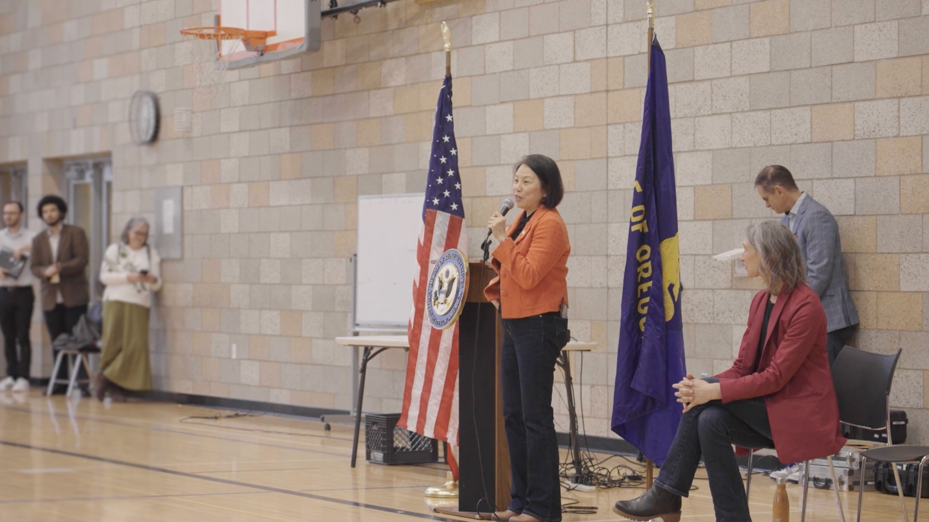 Thuy Tran stands in front of a podium in a school auditorium and speaks into a microphone.