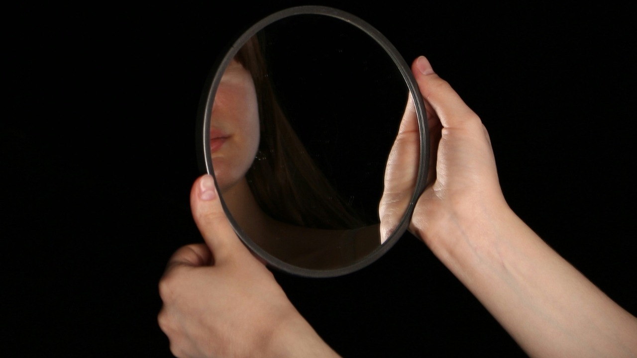 A young woman holding a mirror that reflects part of her mouth