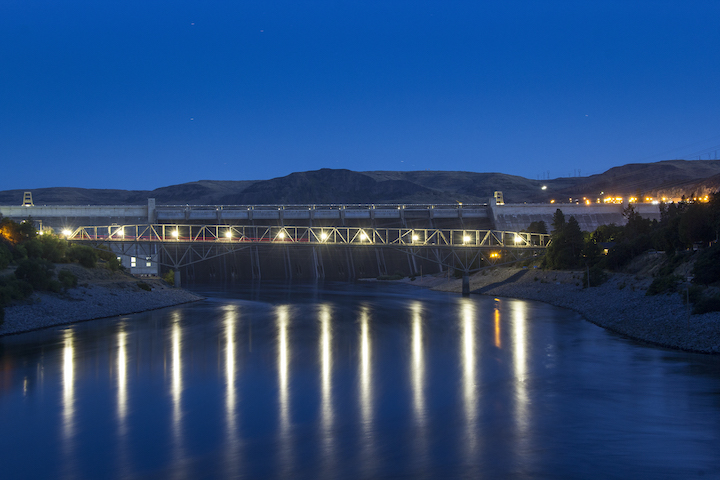 A photo of the Grand Coulee Dam taken at night with lights reflecting off the Columbia River