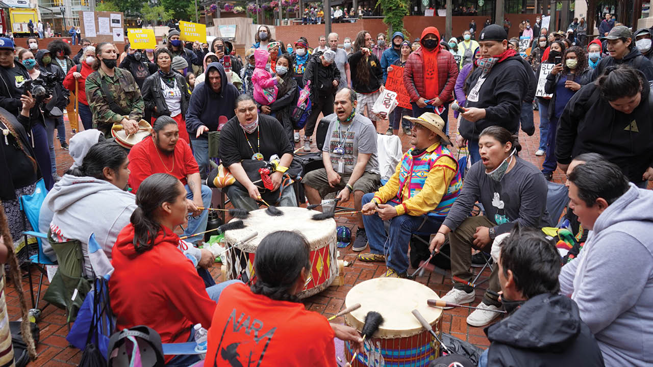 A group of Native American men play drums and sing at a protest at Portland's Pioneer Courthouse Square.