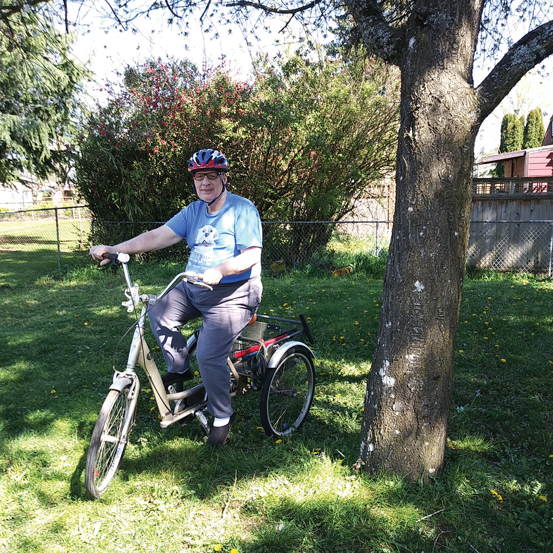 A man rides a three-wheeled bicycle in a back yard